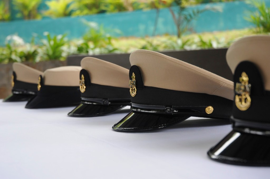 Row of naval officer caps displayed on a table, featuring a combination of khaki and black colors, with gold emblems on the front.